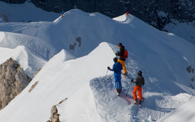 Skiers stand on top of snow-covered mountain peaks.