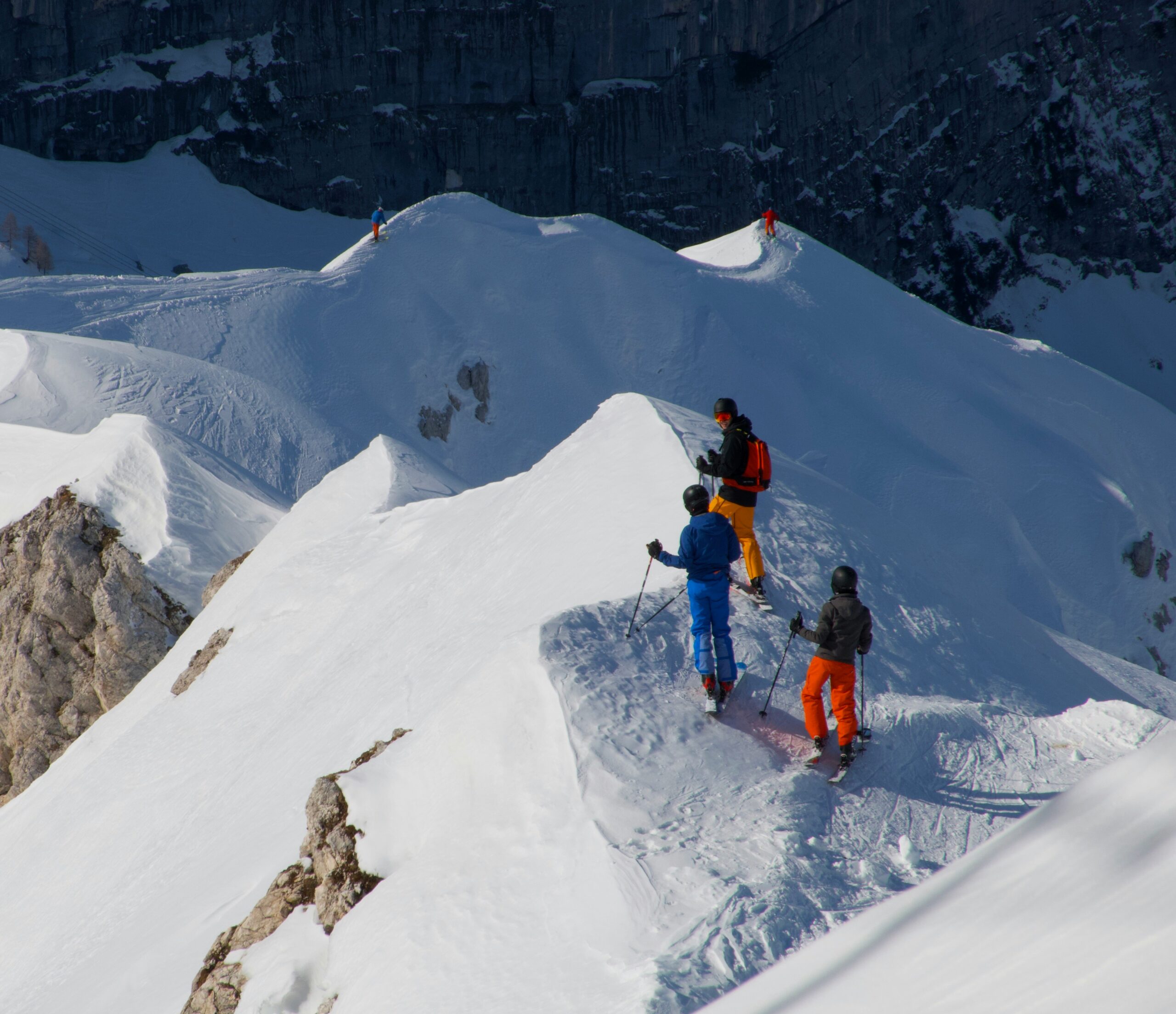 Skiers stand on top of snow-covered mountain peaks.