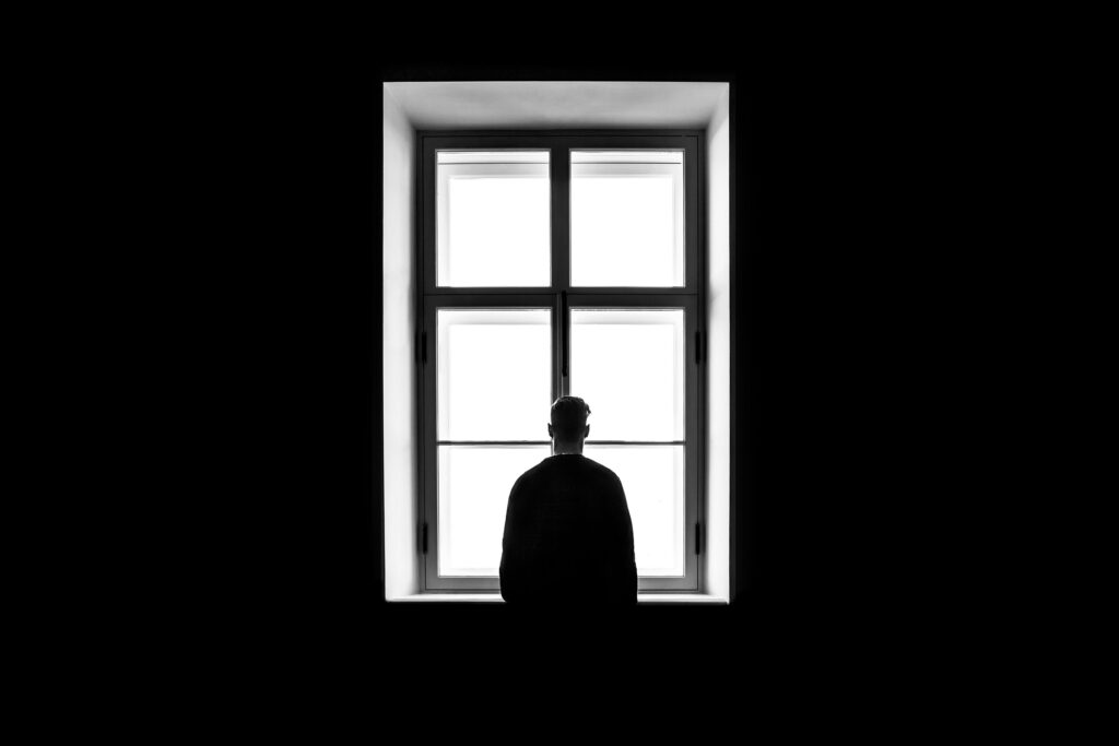 A silhouette of a man standing in front of a window against a black background. Loneliness is becoming an epidemic.